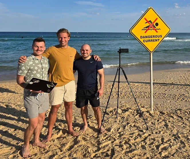 Bryan Pakulski, Alex Piatek and Julian Kovacek beside a coastal camera at Bondi Beach.