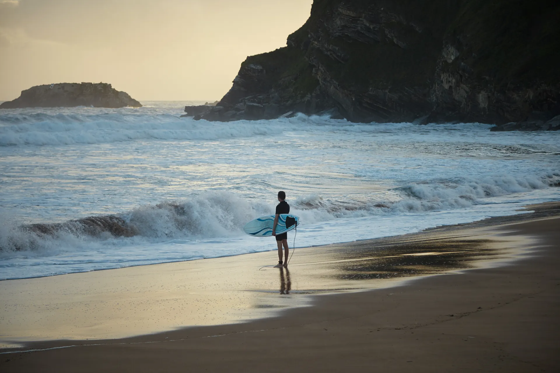 A surfer looking towards the water from a beach.